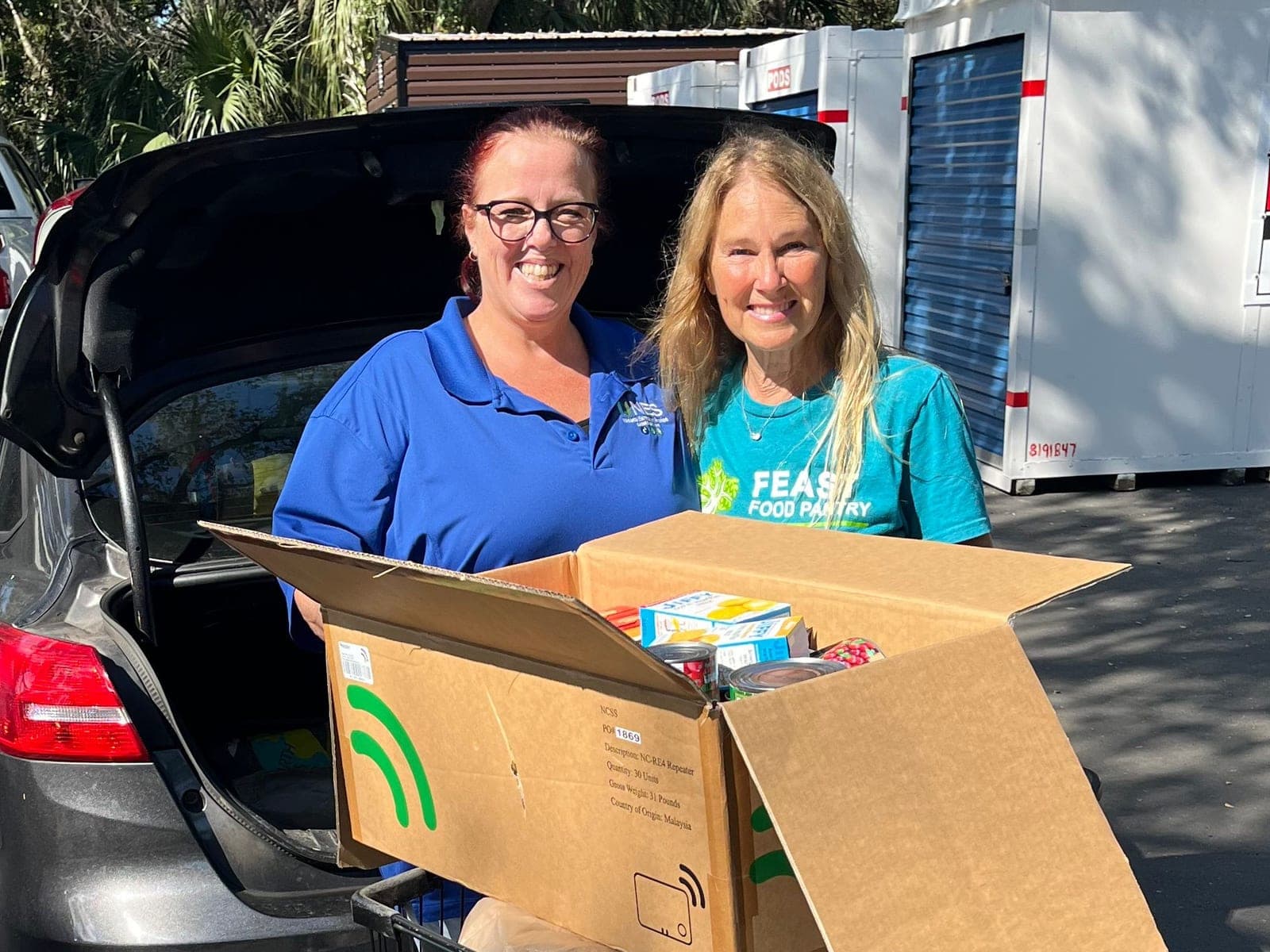 An NES team member and a FEAST Food Pantry volunteer with a box of donated food at the 2025 holiday food drive
